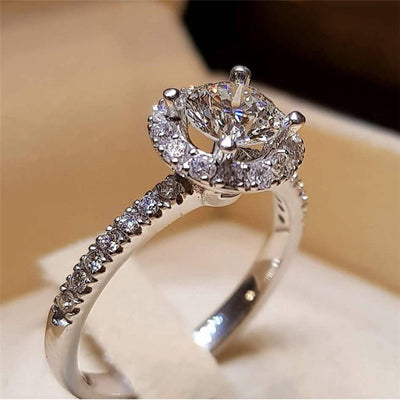 Silver four-prong halo round clear stone ring on cream display
