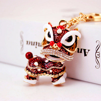 Close-up of a red Chinese lion dance keychain with clear stones and gold-tone hardware.