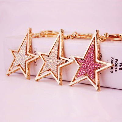 Three gold-tone double-star keychains display iridescent, clear, and pink rhinestones.