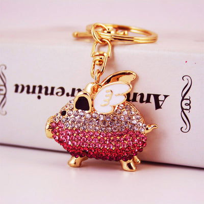 Close-up of a pink rhinestone winged pig charm attached to a gold-tone key ring.
