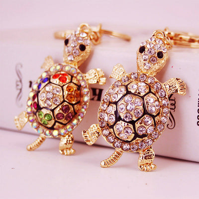 Two gold-tone turtle keychains with multicolor and clear rhinestone shells.