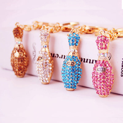 Four rhinestone bowling pin keychains in champagne, white, blue, and pink.