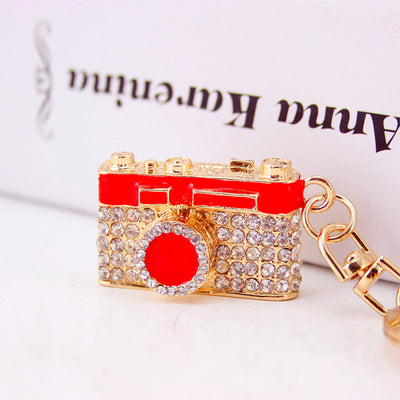 A red camera-shaped keychain covered with clear rhinestones in a front close-up.