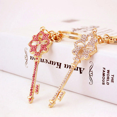 Two gold-tone key charms display pink and white rhinestone fronts beside split rings.