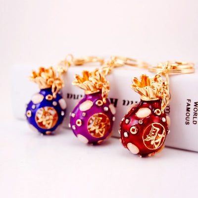 Three money bag keychains in blue, purple, and red displayed together.