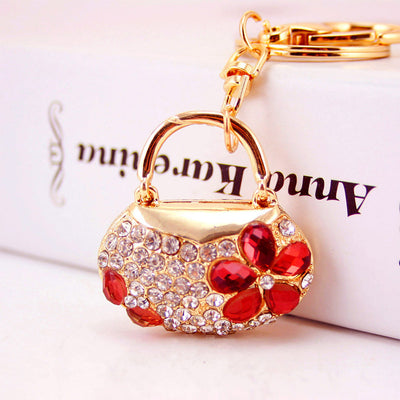 Close-up of a gold-tone handbag charm with clear rhinestones and a red five-petal flower.
