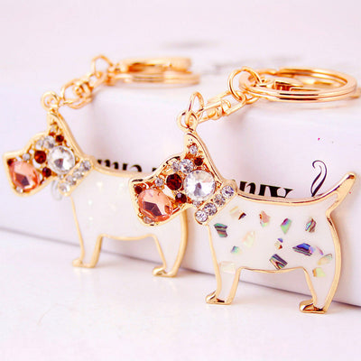 Two gold-tone dog keychains with white enamel and multicolor iridescent inlays.
