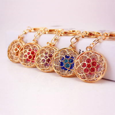 Five round flower keychains with different colored rhinestones arranged in a row.