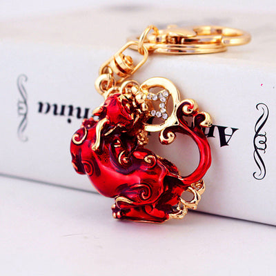 Close-up of a red Pixiu keychain with gold-tone scroll details and clear rhinestones.