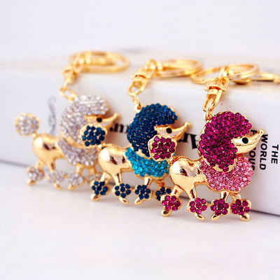 Three gold-tone poodle keychains with pink, blue, and clear rhinestone details.