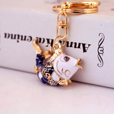 Close-up of a blue and white koi fish keychain resting against a printed box.