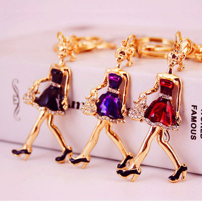 Three gold-tone lady keychains in black, purple, and red dresses arranged together.
