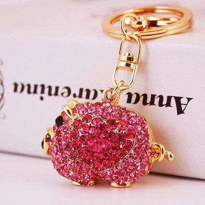 Close-up of a pink rhinestone pig keychain against a pale background.