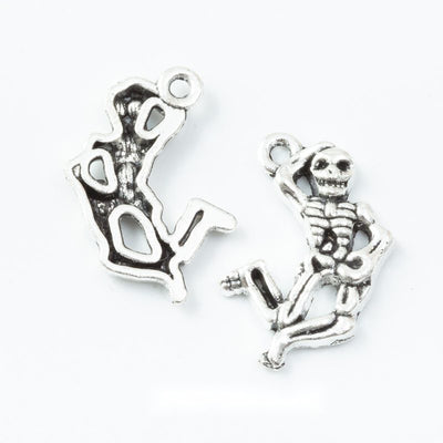 Grouped front view of seated skeleton charms in the available finishes