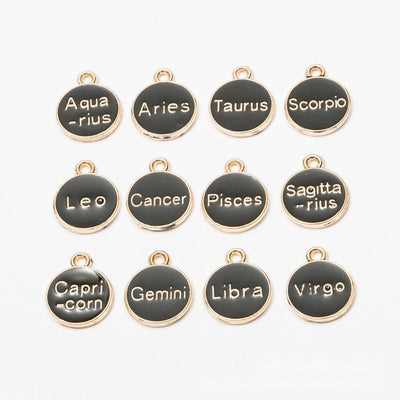 Product view of zodiac charm assortment showing round black enamel discs labeled with the twelve zodiac signs in pale le