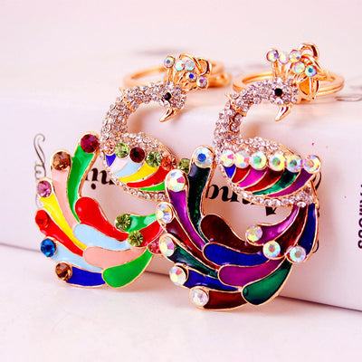 Two gold-tone peacock keychains displayed side by side in light and dark multicolor designs.