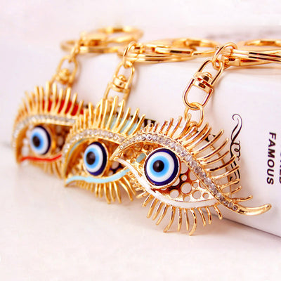 Three gold-tone eye keychains displaying red, blue, and white color details.