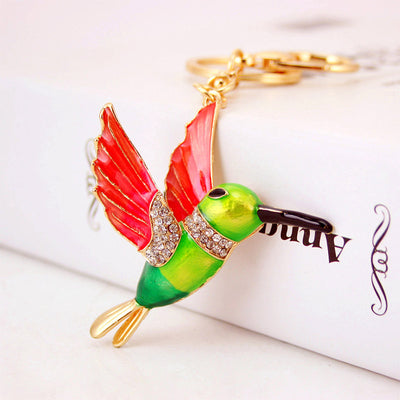 Close-up of a green hummingbird keychain with red wings and clear faceted accents on a white box.