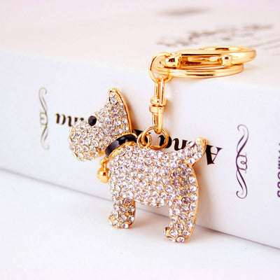 White rhinestone dog keychain resting against a printed book with a gold-tone ring.