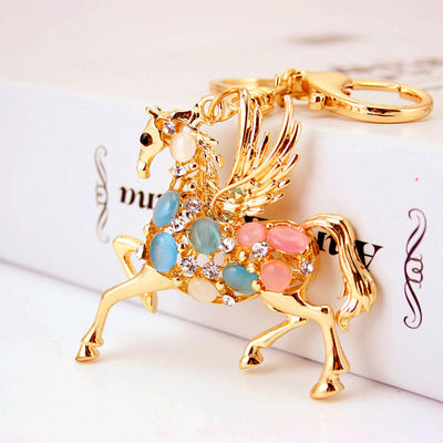 Front close-up of a gold-tone winged horse charm with multicolor oval accents and clear rhinestones.