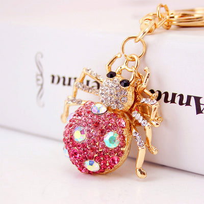 Close view of a pink rhinestone spider hanging from gold-tone keychain hardware.