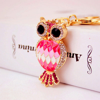 Close-up of a pink owl charm with black eyes, clear stones, and a key ring.