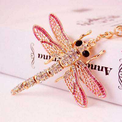 Close-up of a gold-tone dragonfly keychain with pink wing accents and clear rhinestones.