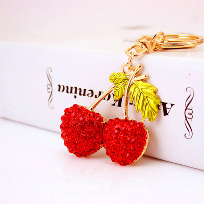 Close-up of a red rhinestone double-cherry charm beside a white box.