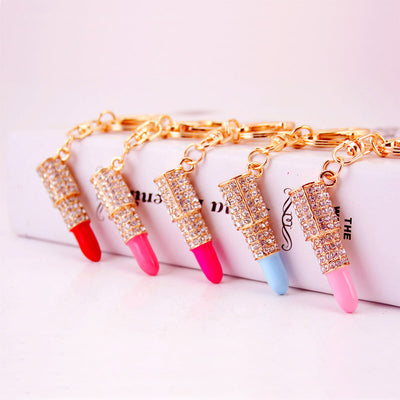 Five lipstick-shaped keychains in red, pink, blue, and light pink beside a white box.