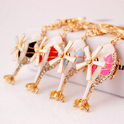 Four gold-tone helicopter keychains in black, red, blue, and pink viewed from above.