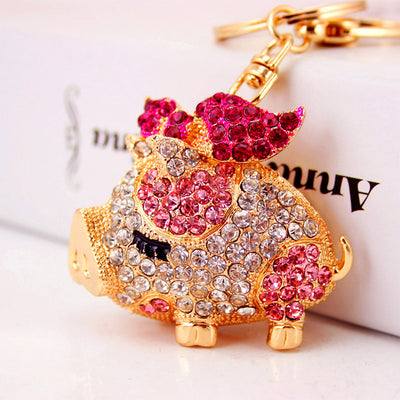 Close-up of a gold-tone pig keychain decorated with clear and pink rhinestones.