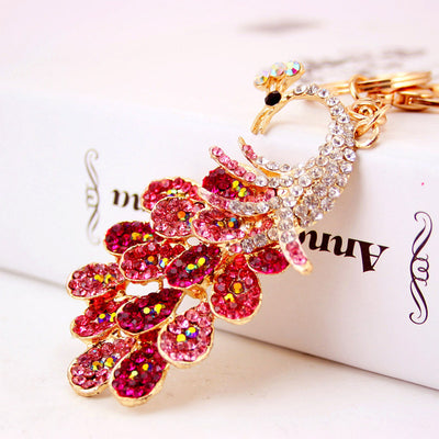 Close-up of a pink rhinestone peacock keychain on a white background.