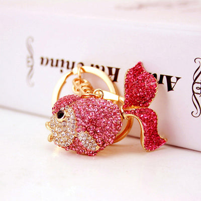 Front view of a pink rhinestone fish charm beside a white box.