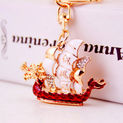 Close view of the red dragon-headed boat charm with white sails and clear stones.