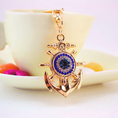 Front view of the rhinestone eye anchor keychain hanging from a cream dish
