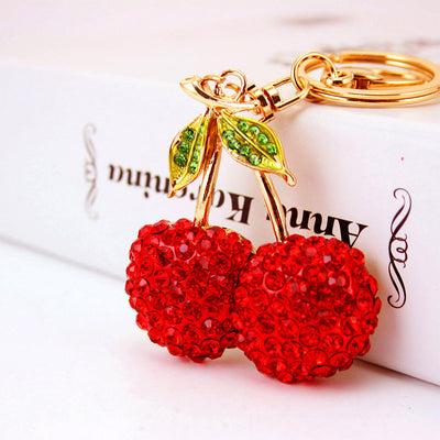 Close-up of red twin-cherry charm with green rhinestone leaves and a gold-tone key ring.