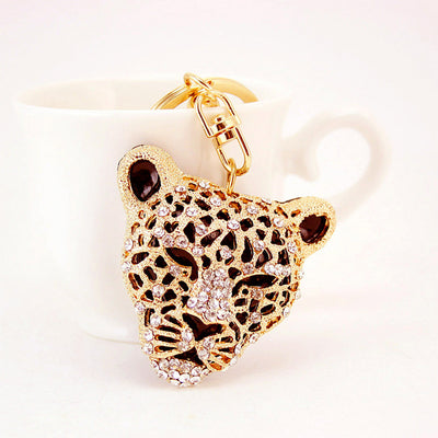 Front view of a gold-tone rhinestone leopard head keychain hanging from a white cup.