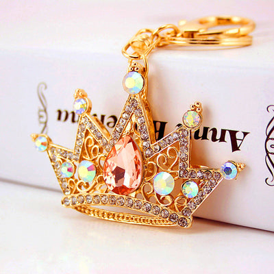 Close-up of a gold-tone crown keychain with a peach teardrop center and iridescent round stones.