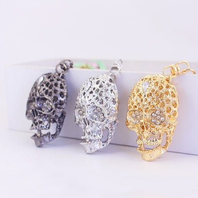 Three openwork skull keychains in gunmetal, silver, and gold finishes.