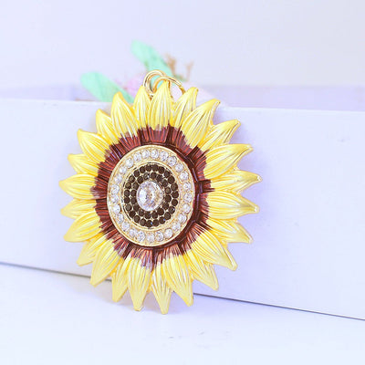 Front close-up of a yellow sunflower pendant with clear and dark faceted accents against a white box.