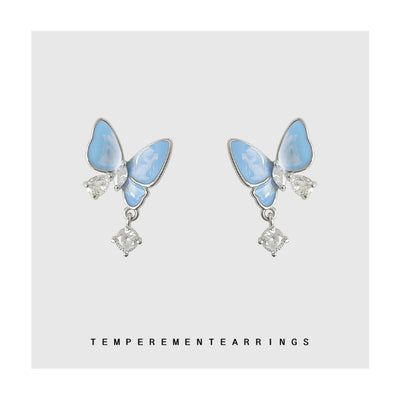 Light blue enamel butterfly drop studs on a gray backdrop