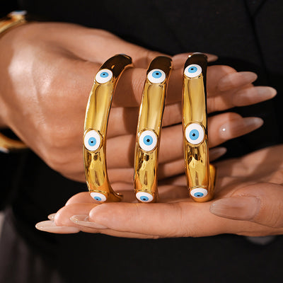 Hands holding three gold evil-eye open cuff bangles