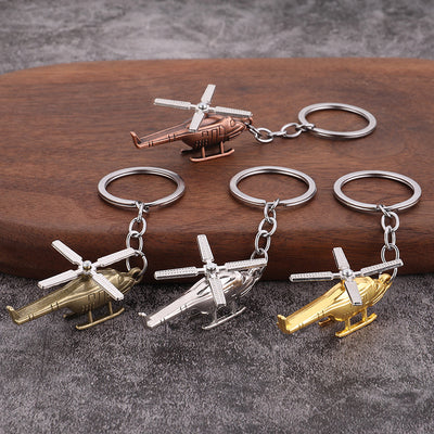 Four helicopter keychains in brass, copper, silver, and gold tones on a wood display.