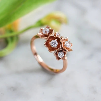 Rose gold flower cluster CZ ring on marble with green leaf