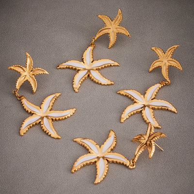 Multiple gold dual starfish drop earrings on textured gray surface