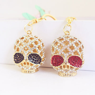 Two gold-tone skull charms with clear stones and contrasting red and black eyes sit side by side.
