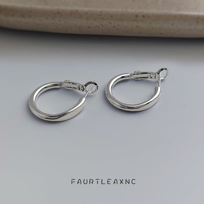 Pair of silver oval hoops on gray surface near ceramic
