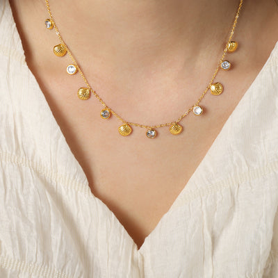 Model wearing gold shell and clear stone charm necklace on white top