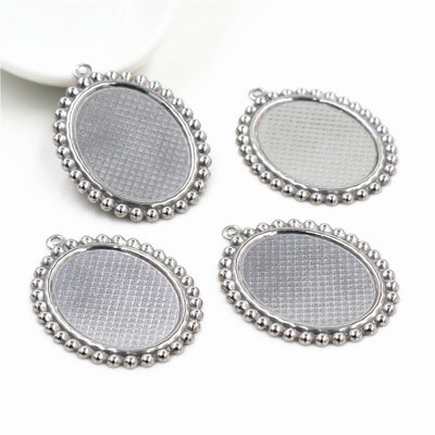 Oval stainless steel cabochon tray with a beaded rim and top loop in a group view on a white background