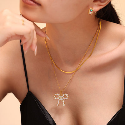 Gold zircon bow pendant layered with snake chain